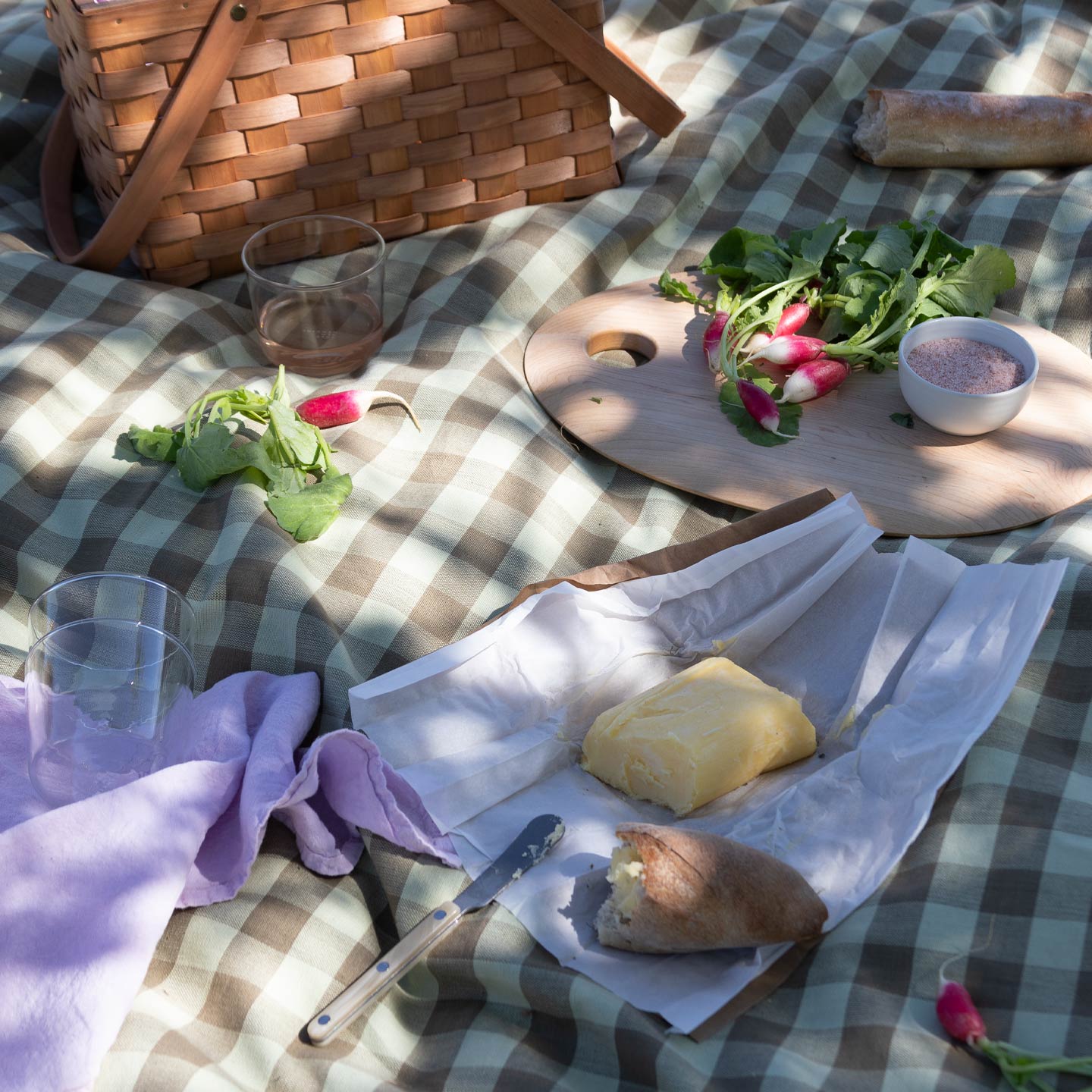 Picnic with Essential Gingham Tablecloth in Olive with basket, turnip, butter, and baguette.