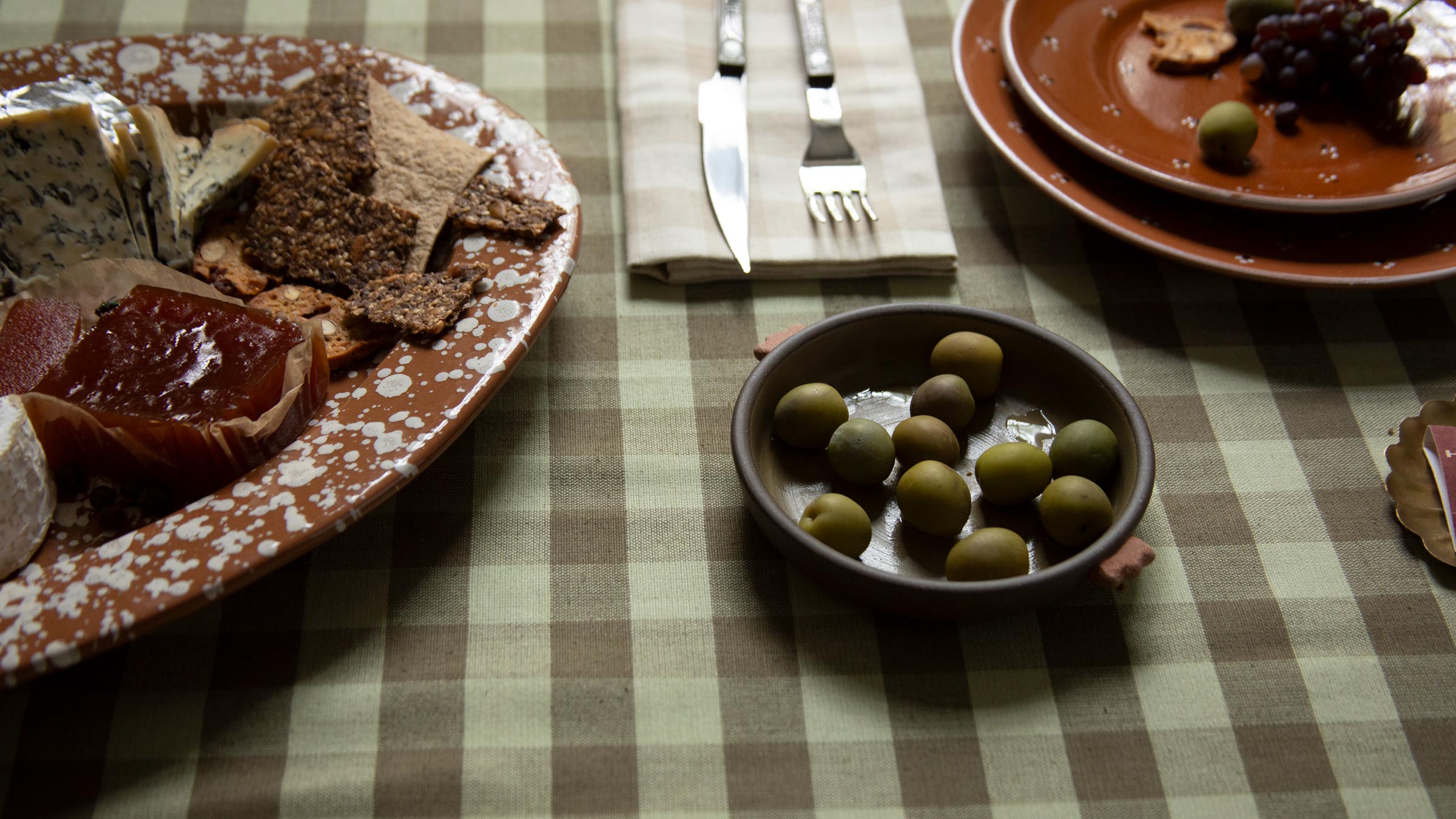 Table setting with plates of food, olives, and cutlery on a checkered tablecloth.