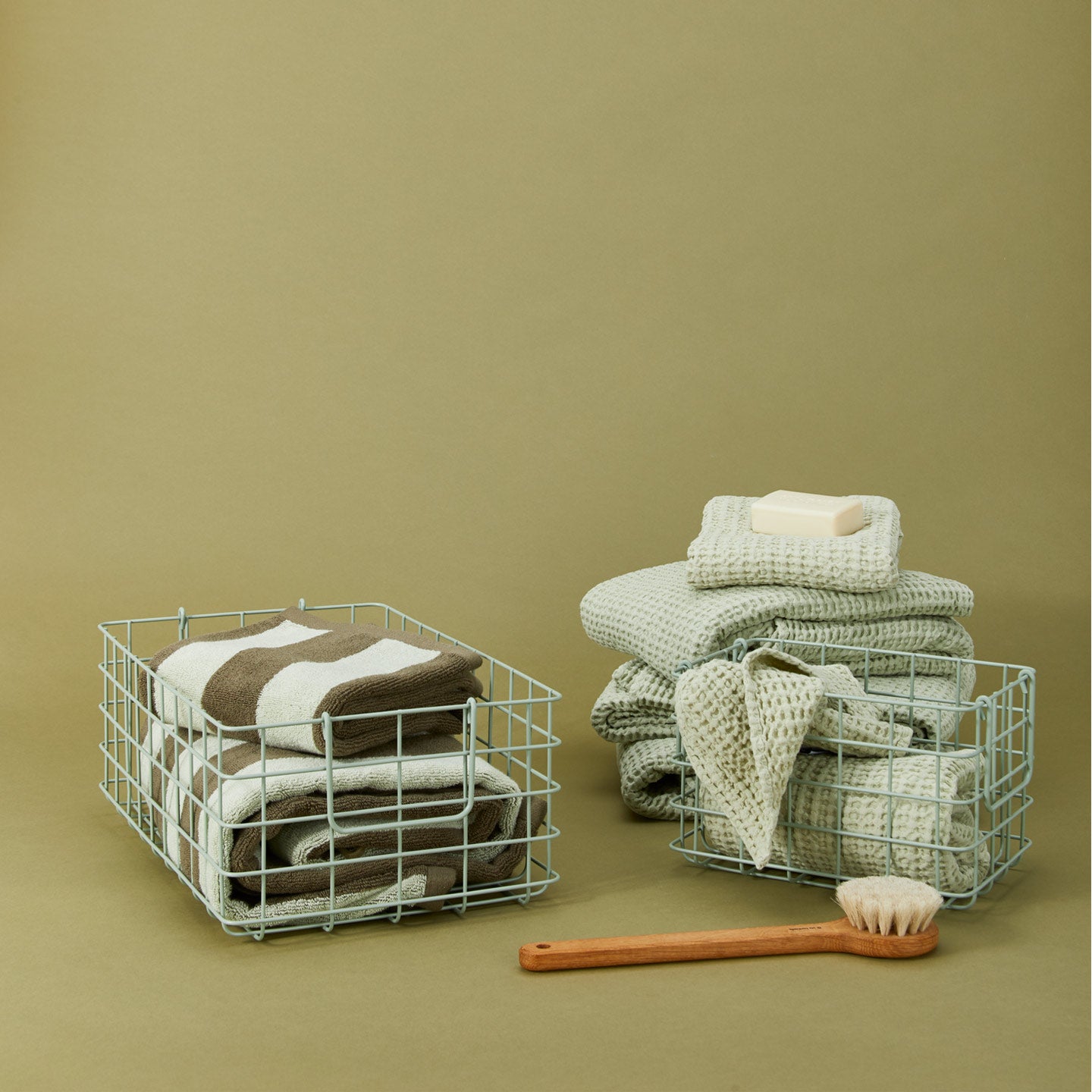 Sage grid baskets, with towes washcloths and a brush on a green background