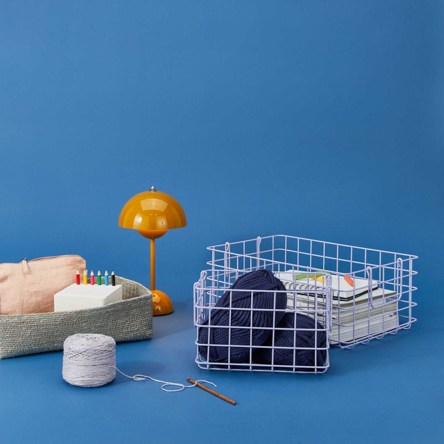 Lilac grid baskets with yarn and stationery. a basket with art supplies, and an orange lamp