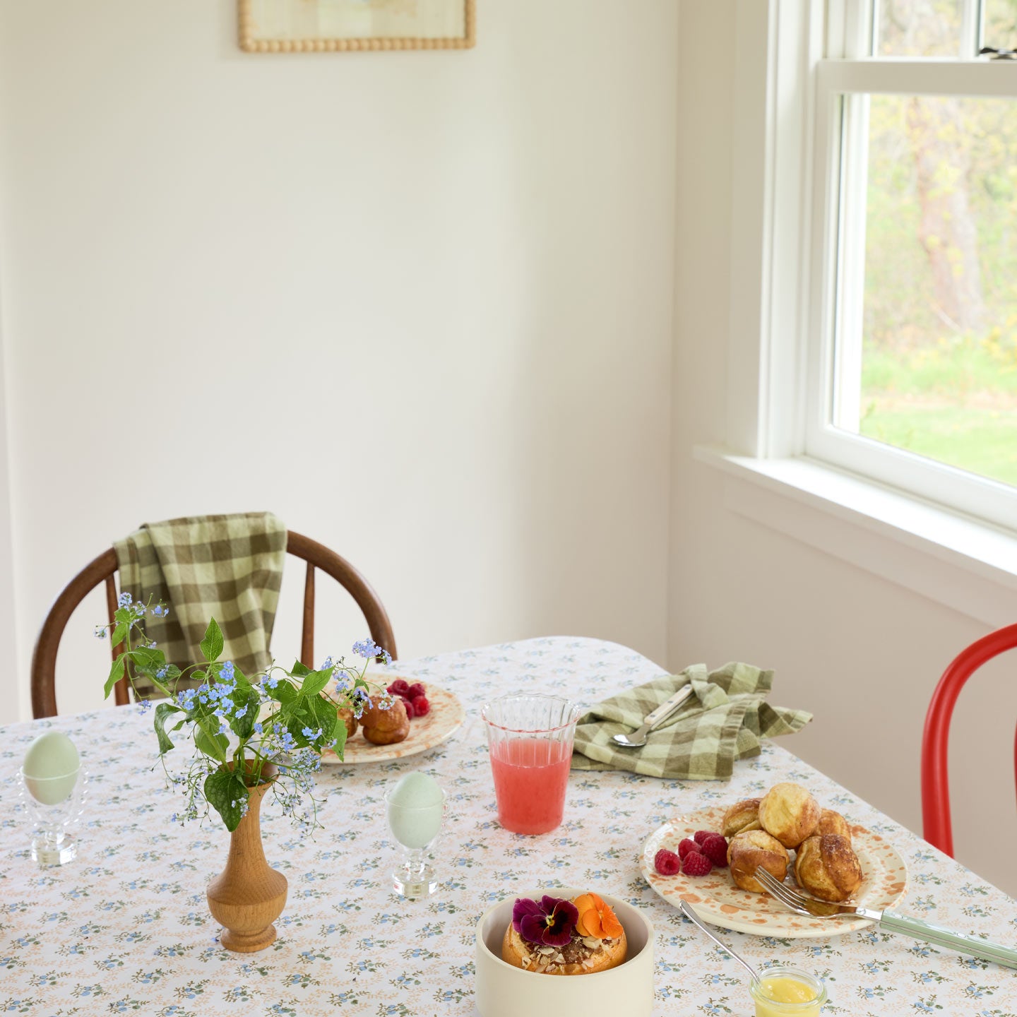 Dining table set with plates of food, a glass of pink drink, and flowers in a room with a window.