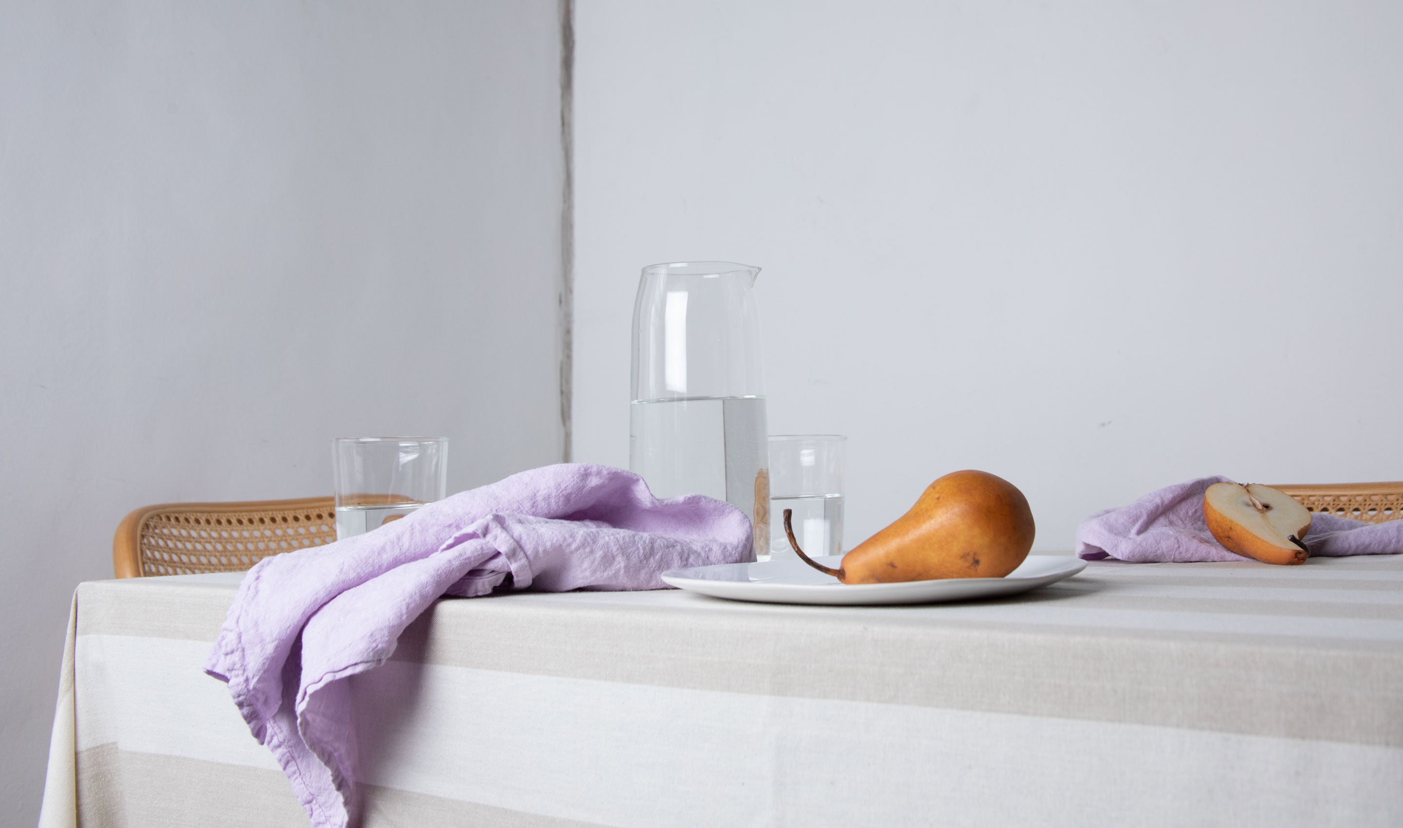 dining table set with lilac linen napkins, striped tablecloth, plates, glasses, pitcher and styled with pears