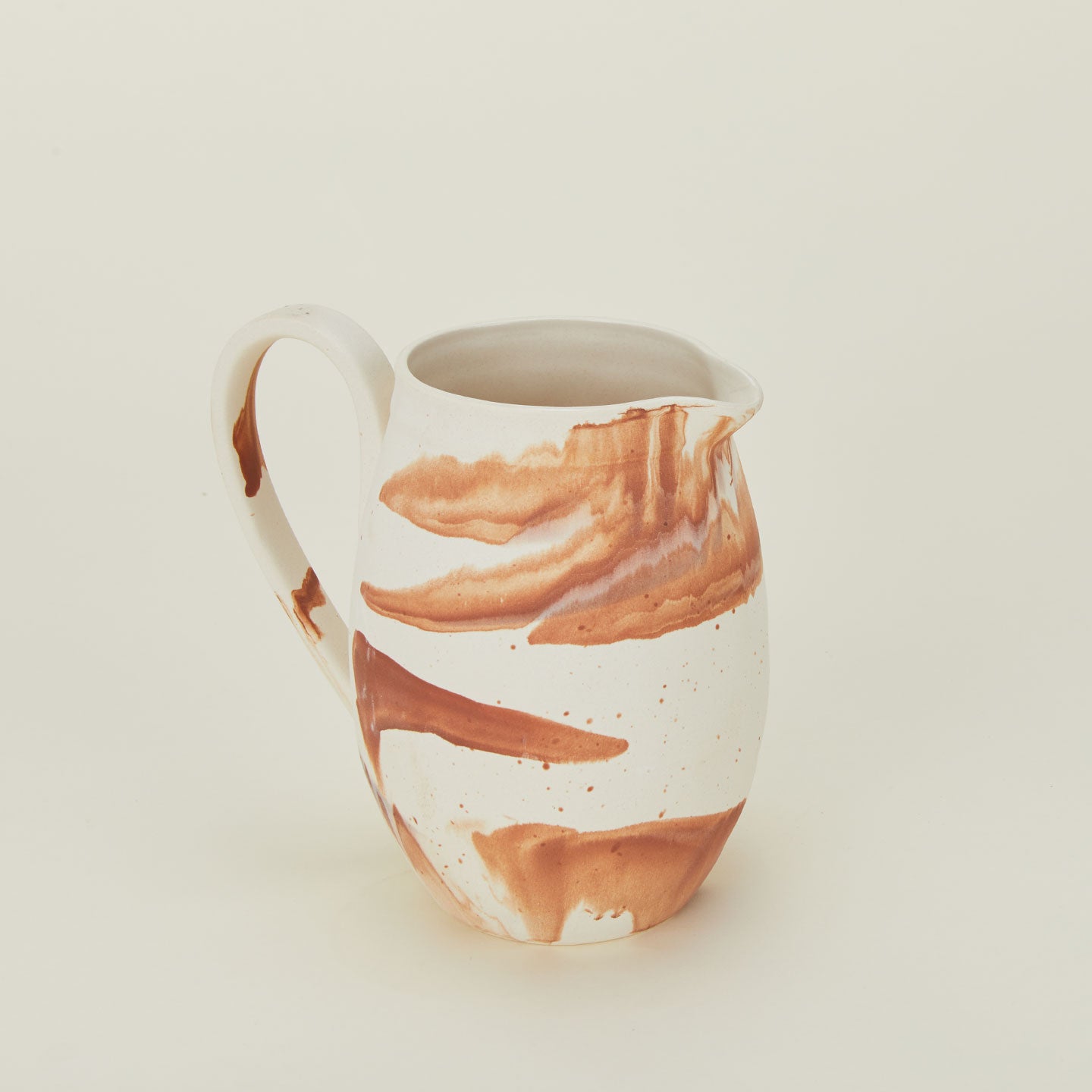 Close up of white stoneware pitcher with terracotta orange marbled glaze.
