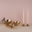 A trio of footed bowls and pair of candle holders, all in Brass, with white taper candles. Styled with a butterfly.