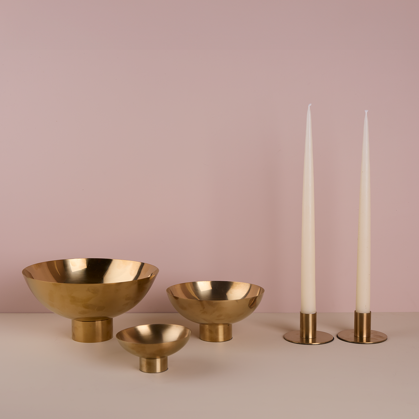 A trio of footed bowls and pair of candle holders, all in Brass, with white taper candles.