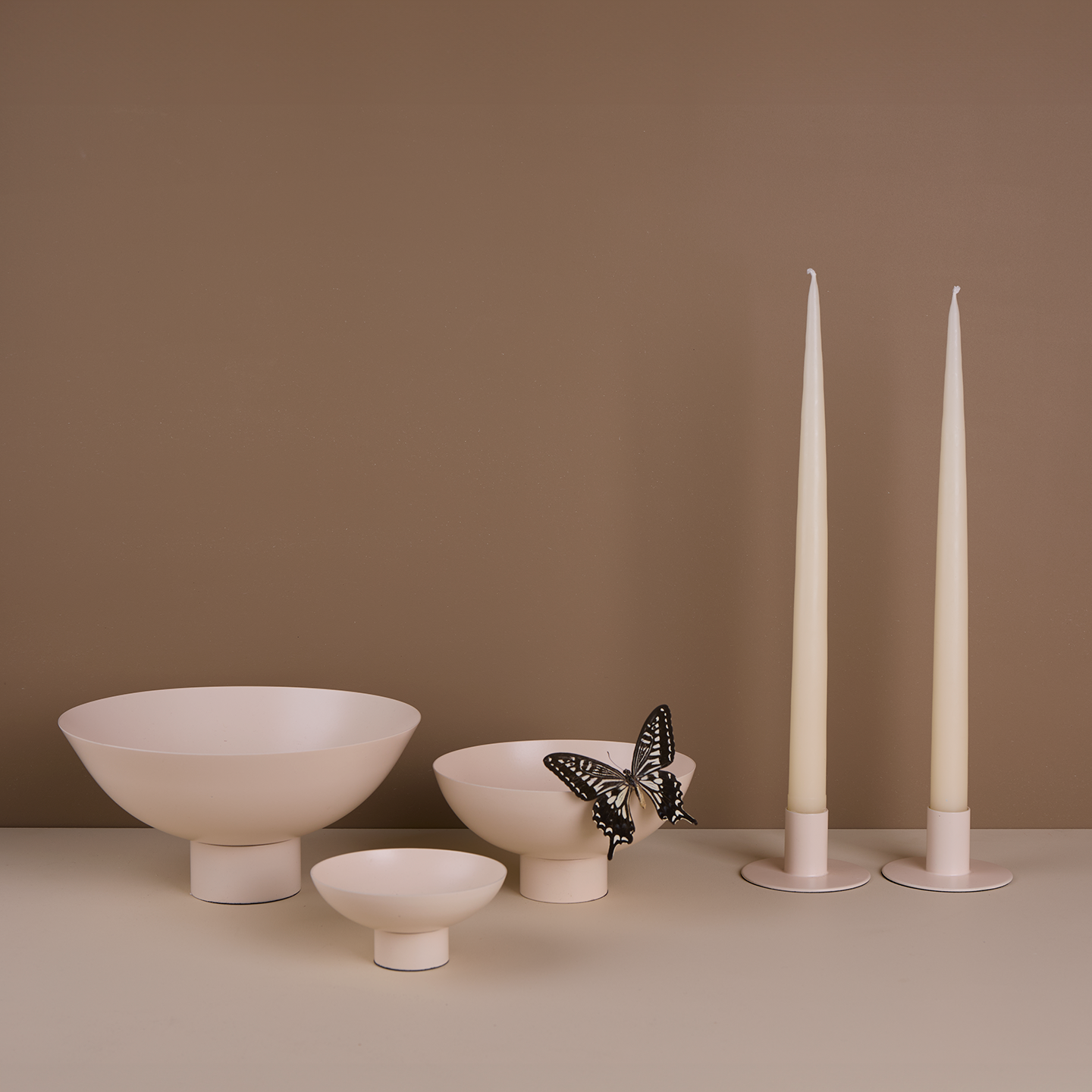 A trio of footed bowls and pair of candle holders, all in Ivory, with ivory taper candles. Styled with a butterfly.