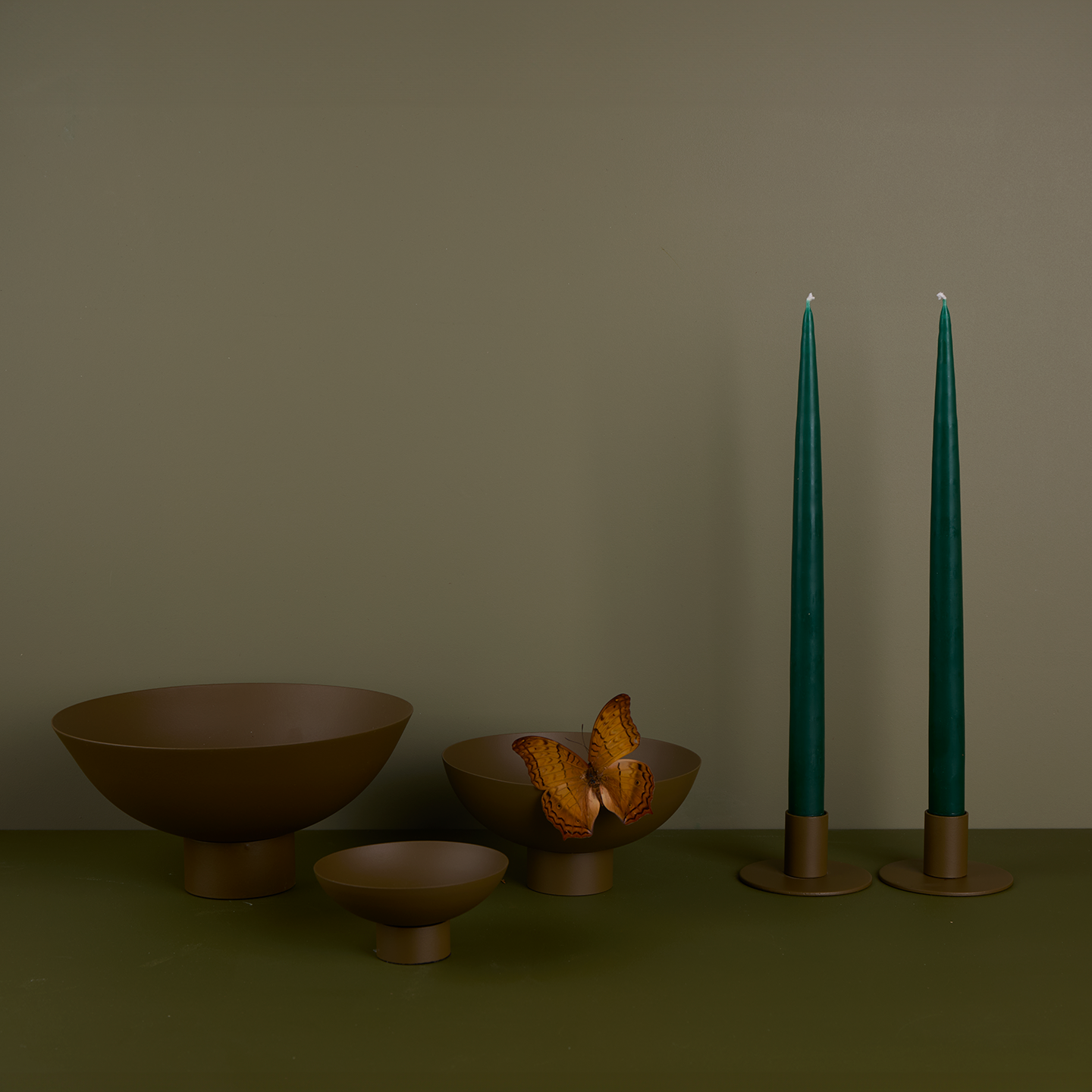 A trio of footed bowls and pair of candle holders, all in Olive, with green taper candles. Styled with a butterfly.