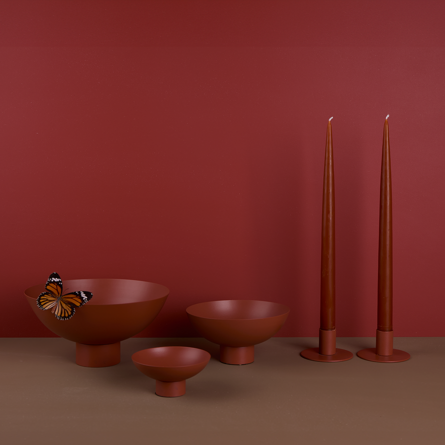 A trio of footed bowls and pair of candle holders, all in Terracotta, with red-orange taper candles. Styled with a butterfly.