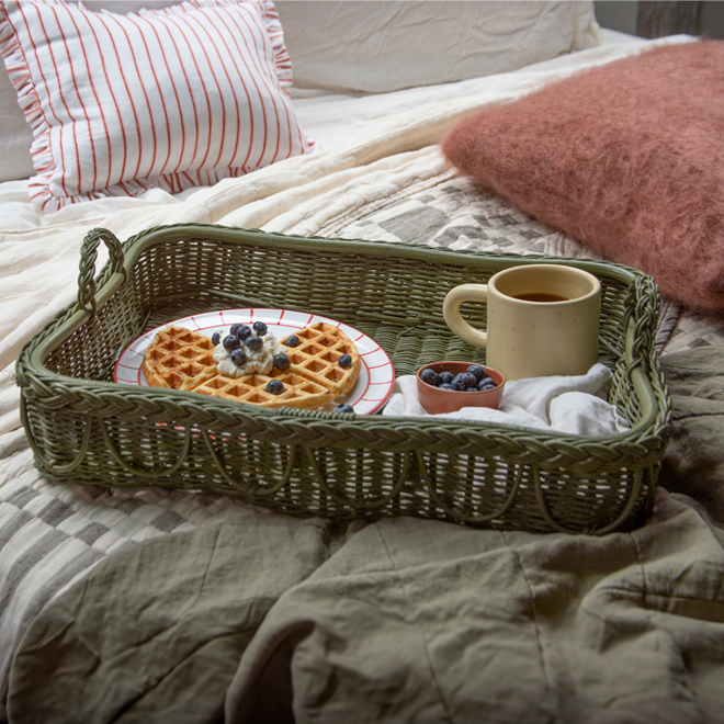 Wicker tray with waffles, berries, and a mug on a bed