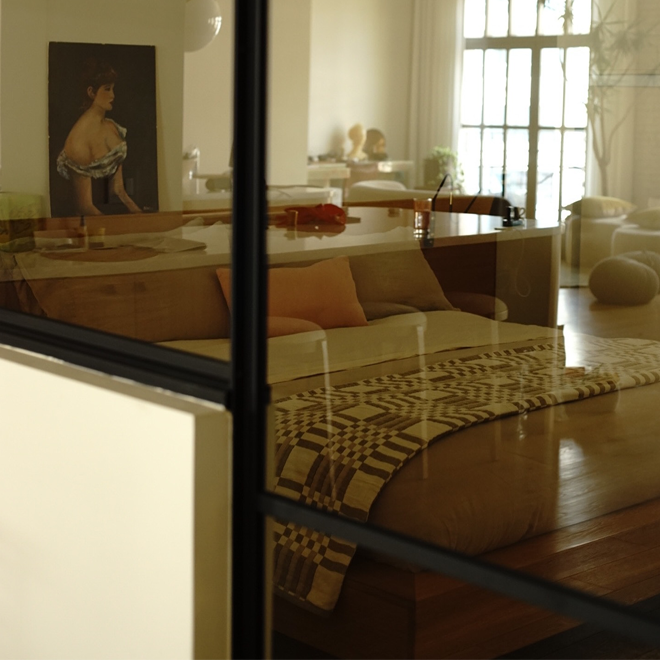 Modern loft viewed through a glass panel with a bed, table, and decorative items.