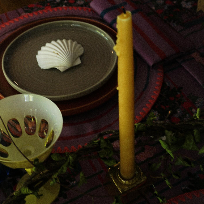 Maximalist tablescape with a beeswax candle on a stand and a shell on a plate in the background