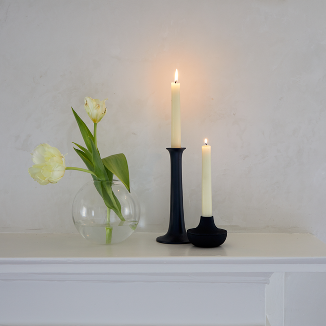 Two candles in black holders and a clear vase with white tulips on a white mantel.