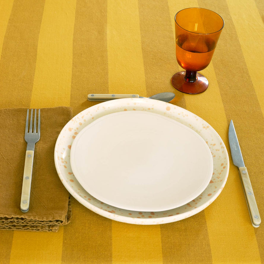 Placesetting on Essential Striped Tablecloth in Mustard and Bronze with bronze napkin and flatware.