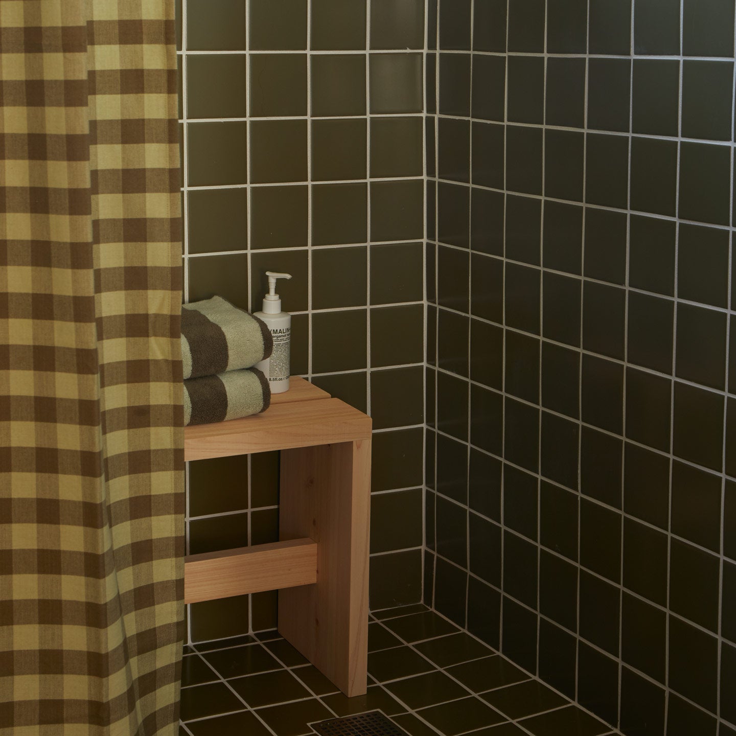 Essential Gingham Shower Curtain in Olive in olive tiled shower with bench and striped bath towels and soap.