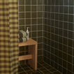 Essential Gingham Shower Curtain in Olive in olive tiled shower with bench and striped bath towels and soap.