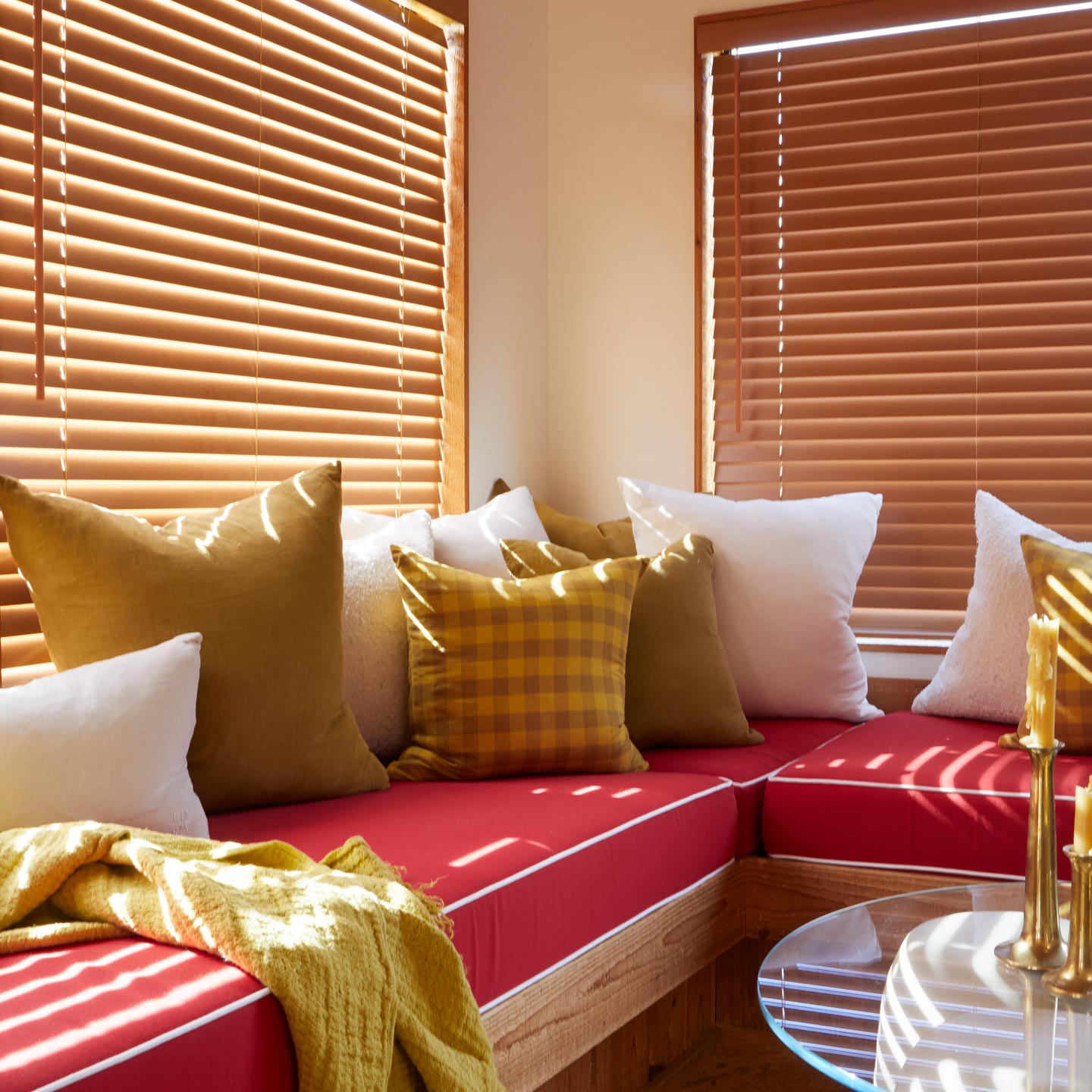 Red sofa with colorful cushions in a room with wooden blinds.