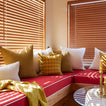 Red sofa with colorful cushions in a room with wooden blinds.