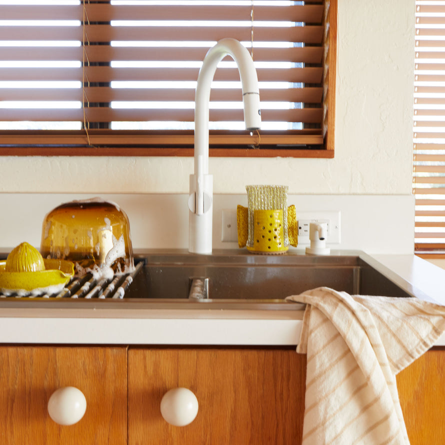 Modern kitchen sink with yellow glass items and wooden cabinets.