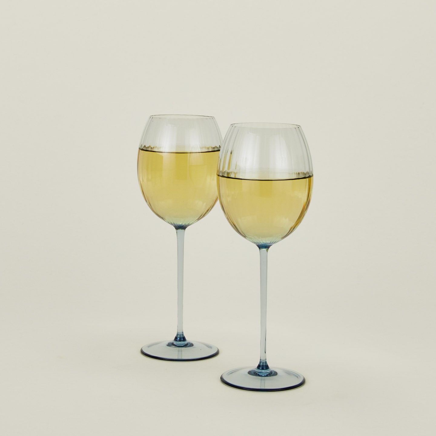 Set of two ribbed blue wine glasses with white wine.