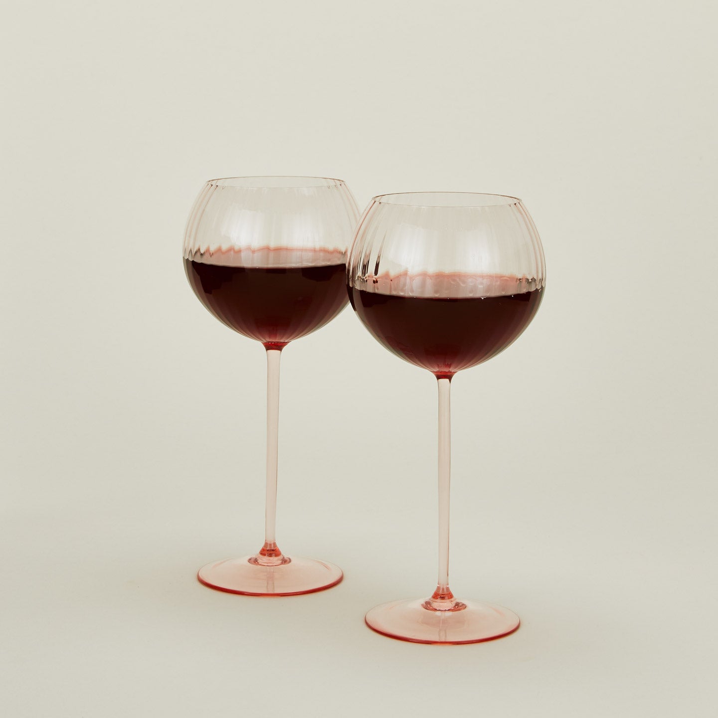Set of two ribbed blush wine glasses with red wine.