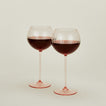 Set of two ribbed blush wine glasses with red wine.