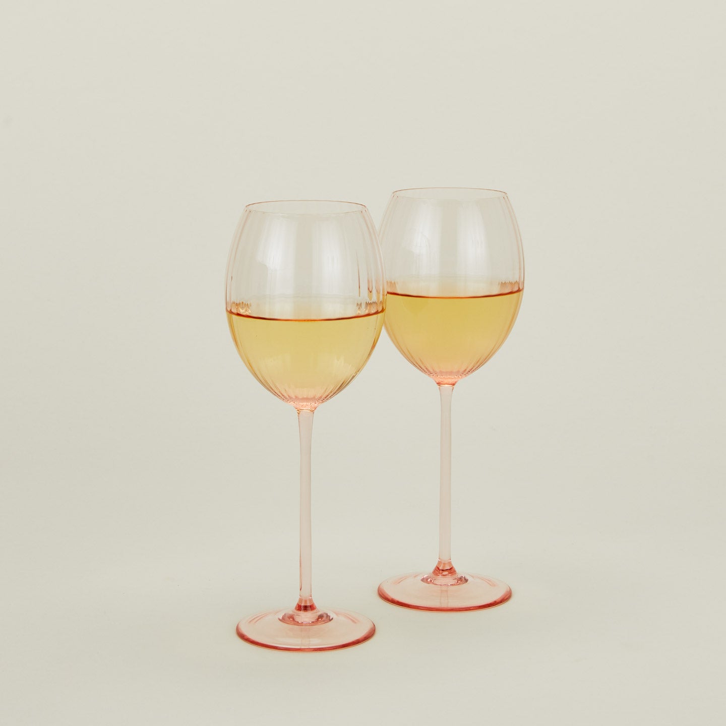 Set of two ribbed blush wine glasses with white wine.