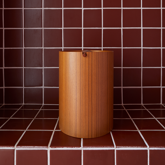 Wooden cylindrical waste can against a red tiled wall