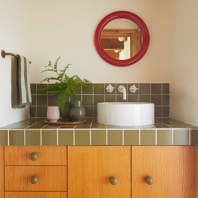 Bathroom with wooden vanity, white sink, and red mirror.