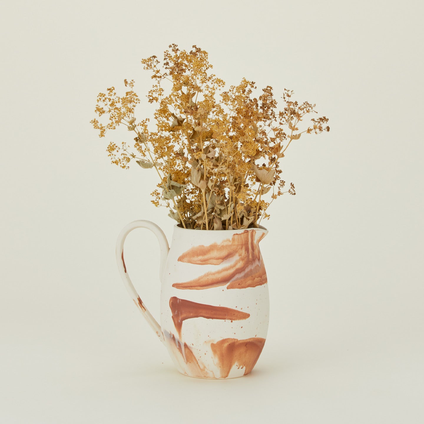 White stoneware pitcher with terracotta orange marbled glaze, with flowers.