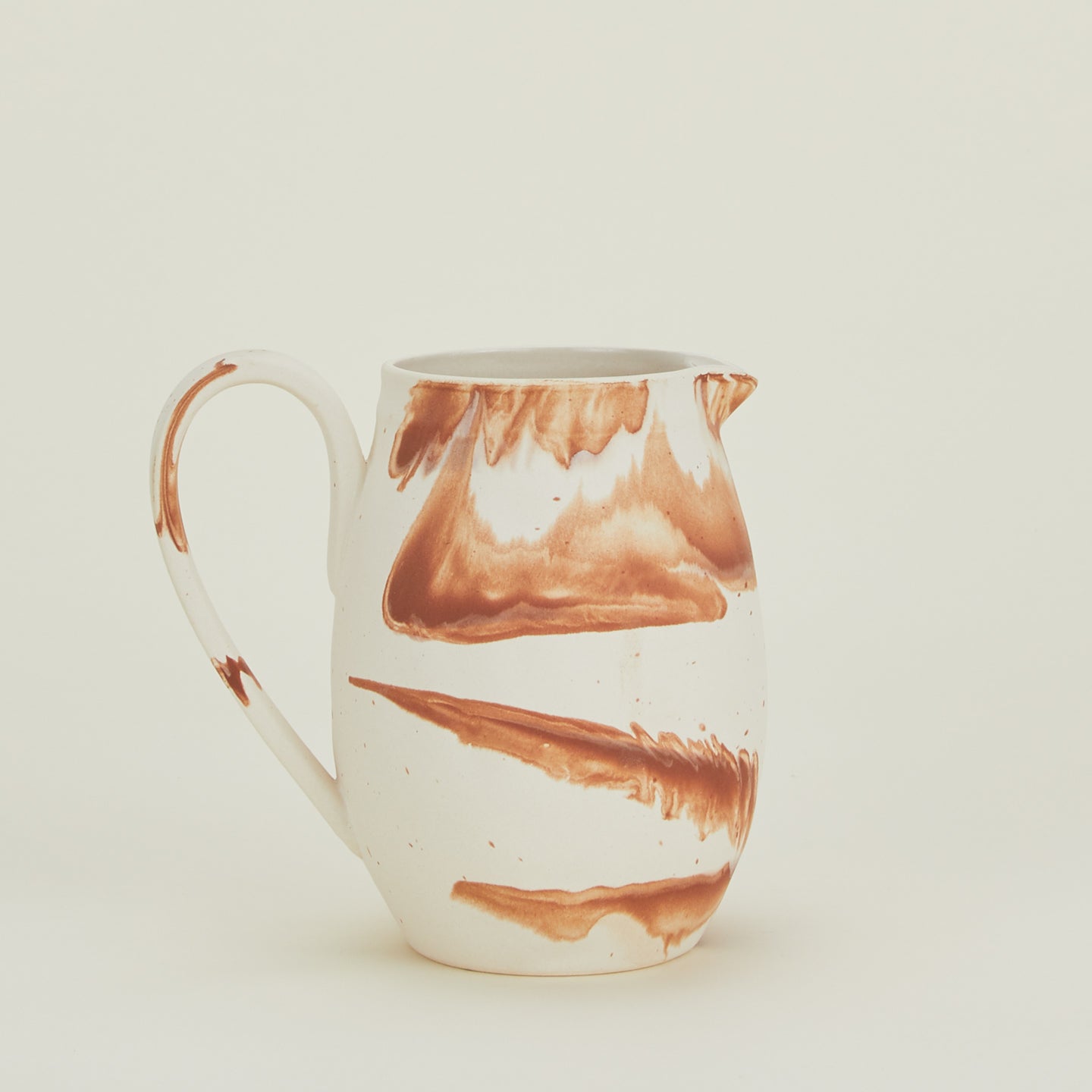 White stoneware pitcher with terracotta orange marbled glaze.