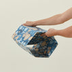 Hands unfolding collapsible marbled hexagon wastebasket.