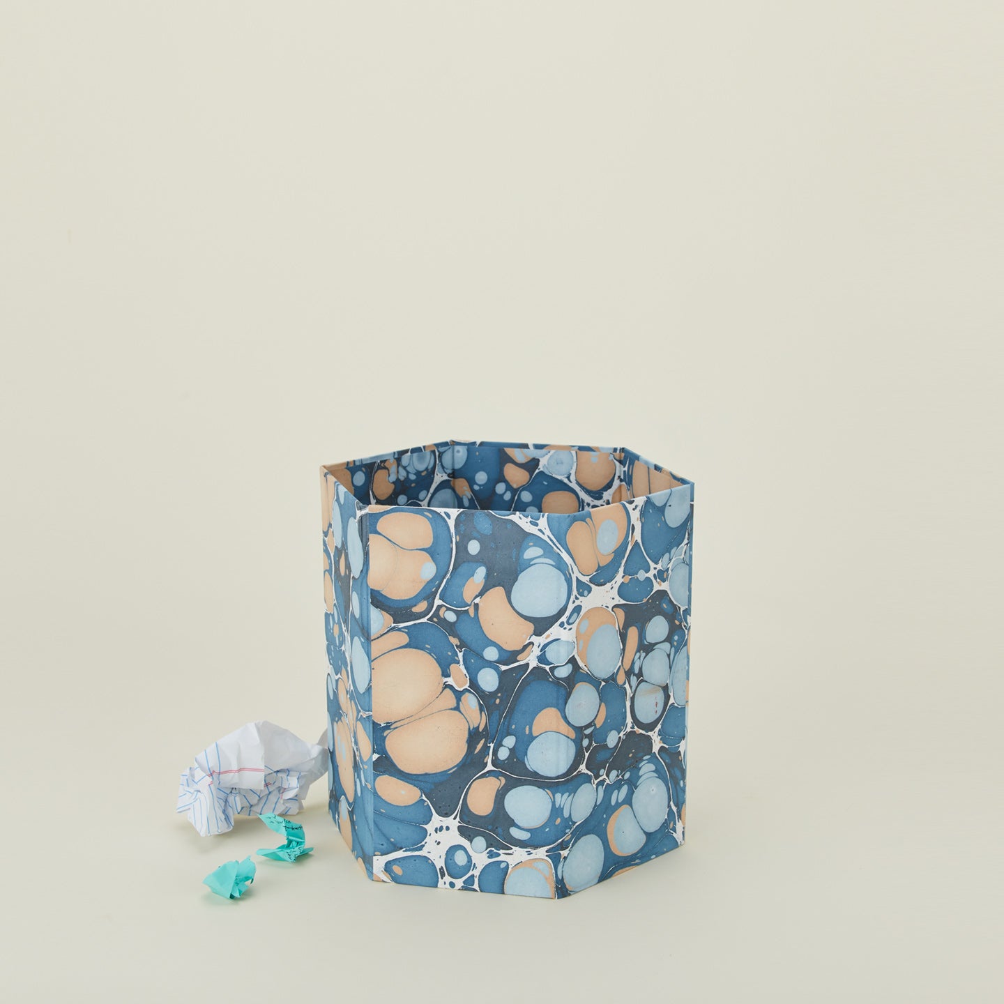 Marbled hexagon wastebasket in cool tones with balled-up paper.