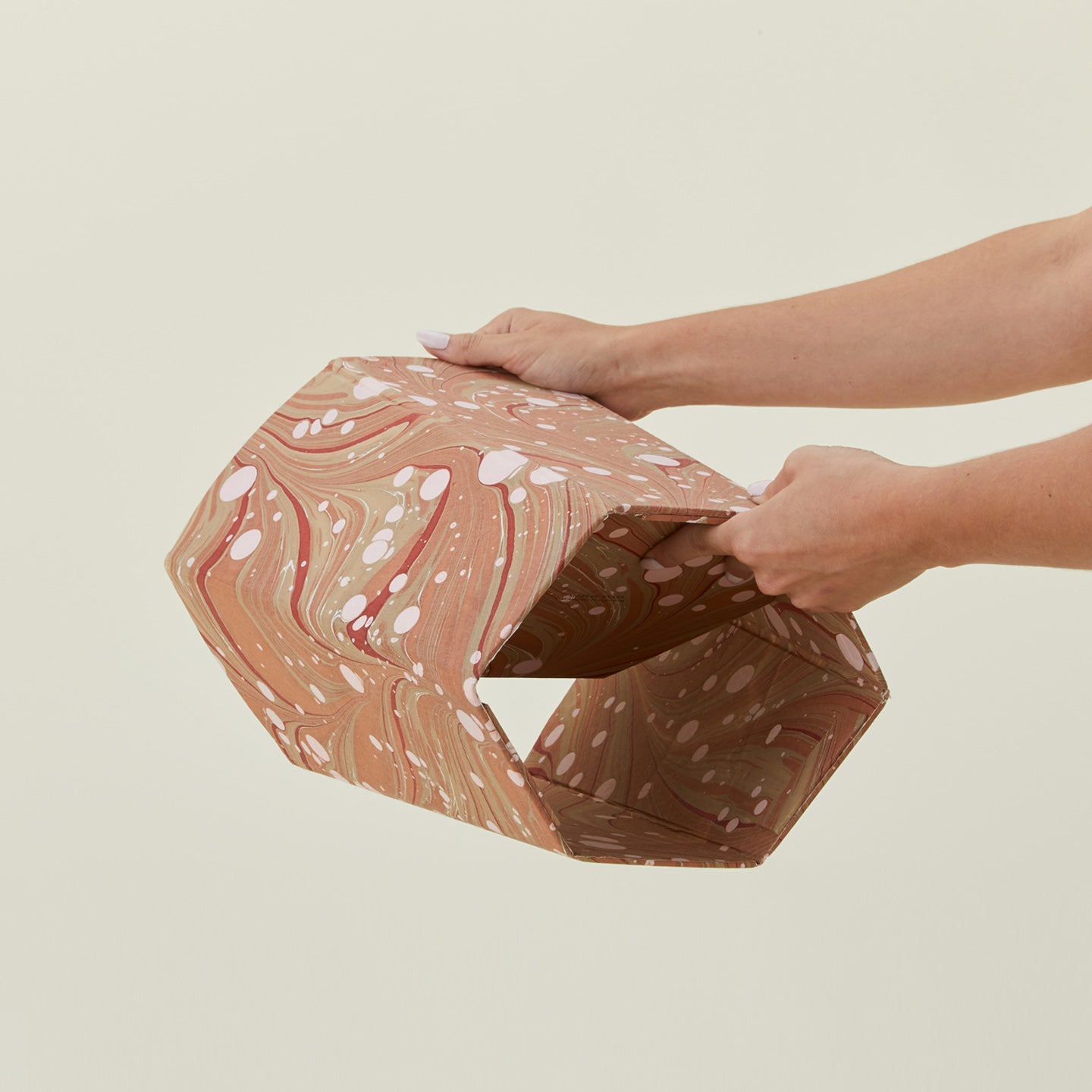 Hands unfolding collapsible marbled scalloped wastebasket.