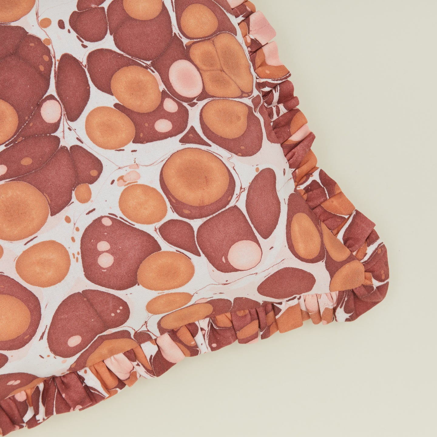 Detail of marbled cotton ruffled pillow in warm tones.