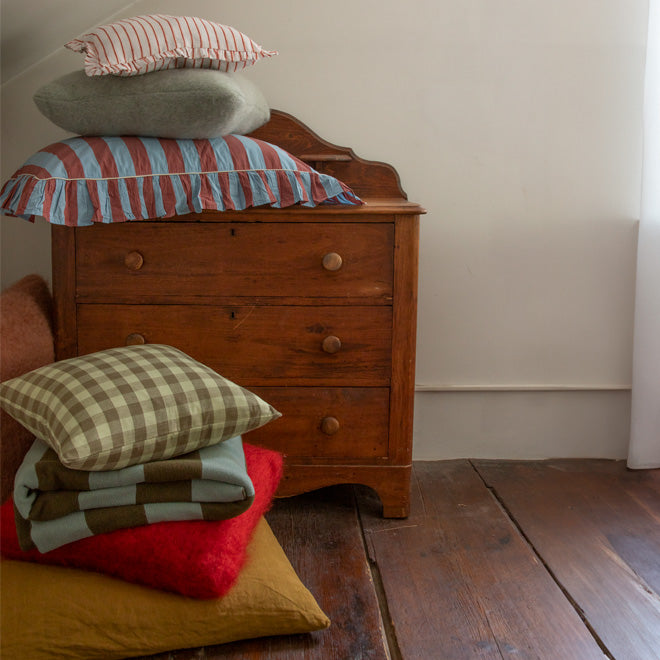 Wooden dresser with a stack of pillows of various colors, materials, shapes, and patterns
