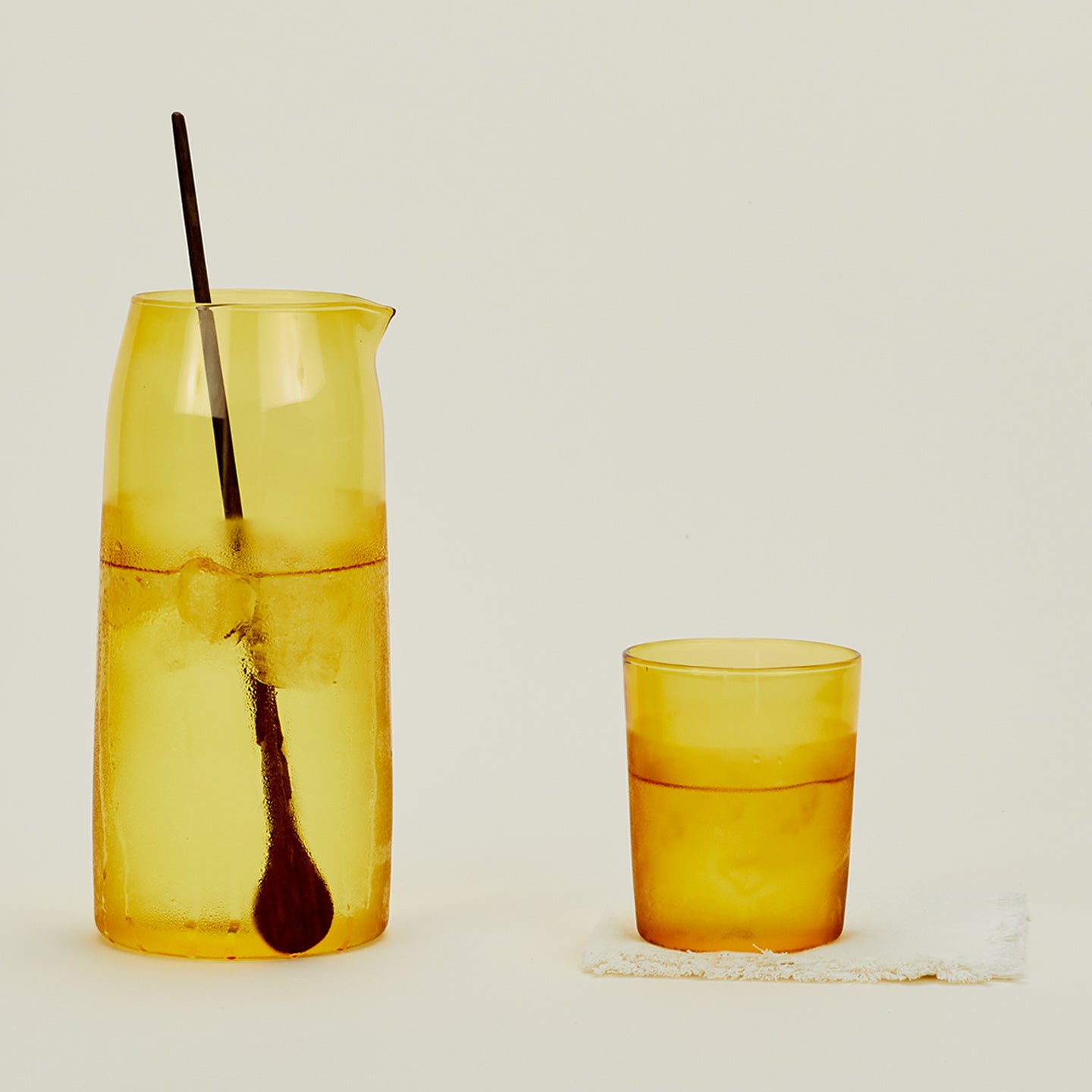 Essential Glassware Pitcher in Amber, filled with ice water, along with a drinking glass and stirring spoon.