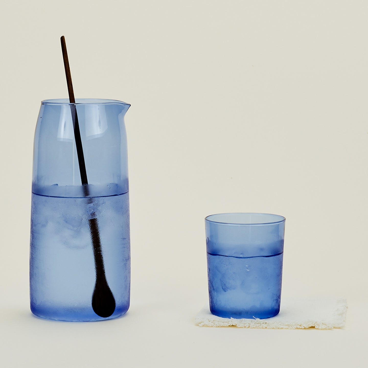 Essential Glassware Pitcher in Blue, filled with ice water, along with a drinking glass and stirring spoon.