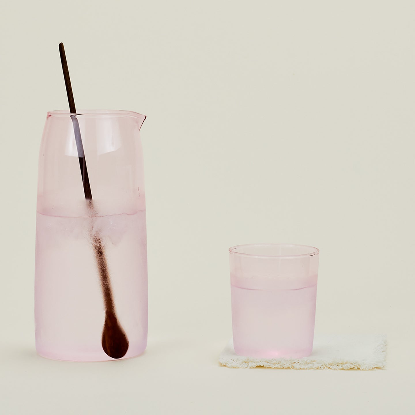 Essential Glassware Pitcher in Blush, filled with ice water, along with a drinking glass and stirring spoon.
