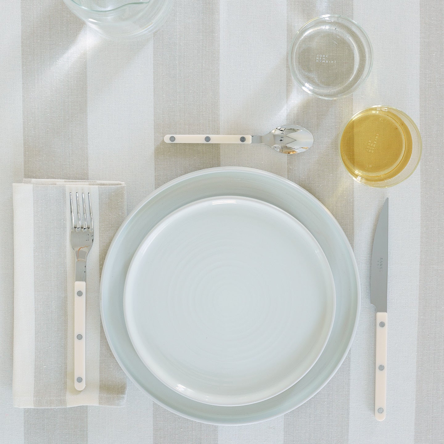 Placesetting with Essential Dinner Plate in Bone on ivory striped tablecloth.