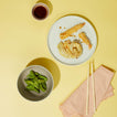 Plated tempura with edamame and chopsticks on a yellow background with xs bowl in blush and blush napkin.