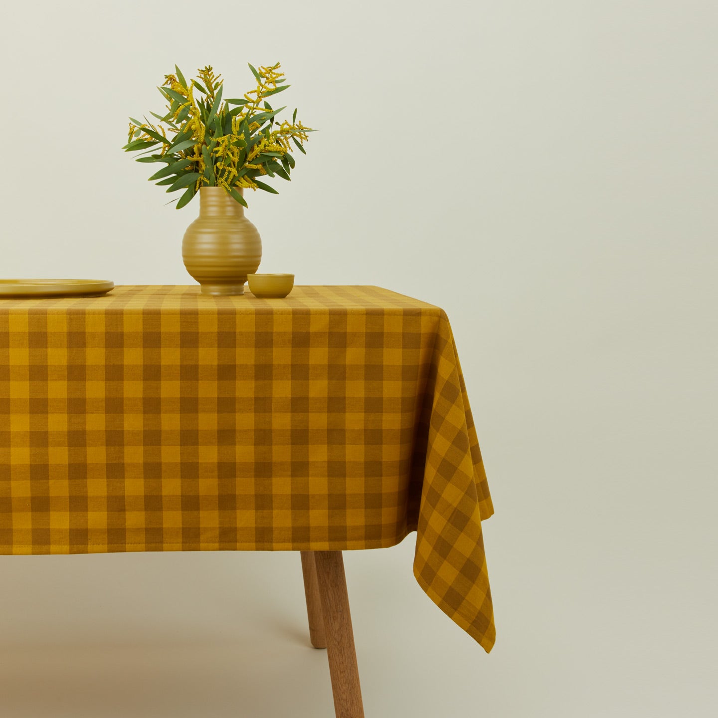 Essential Gingham tablecloth in mustard/bronze on a table with florals.