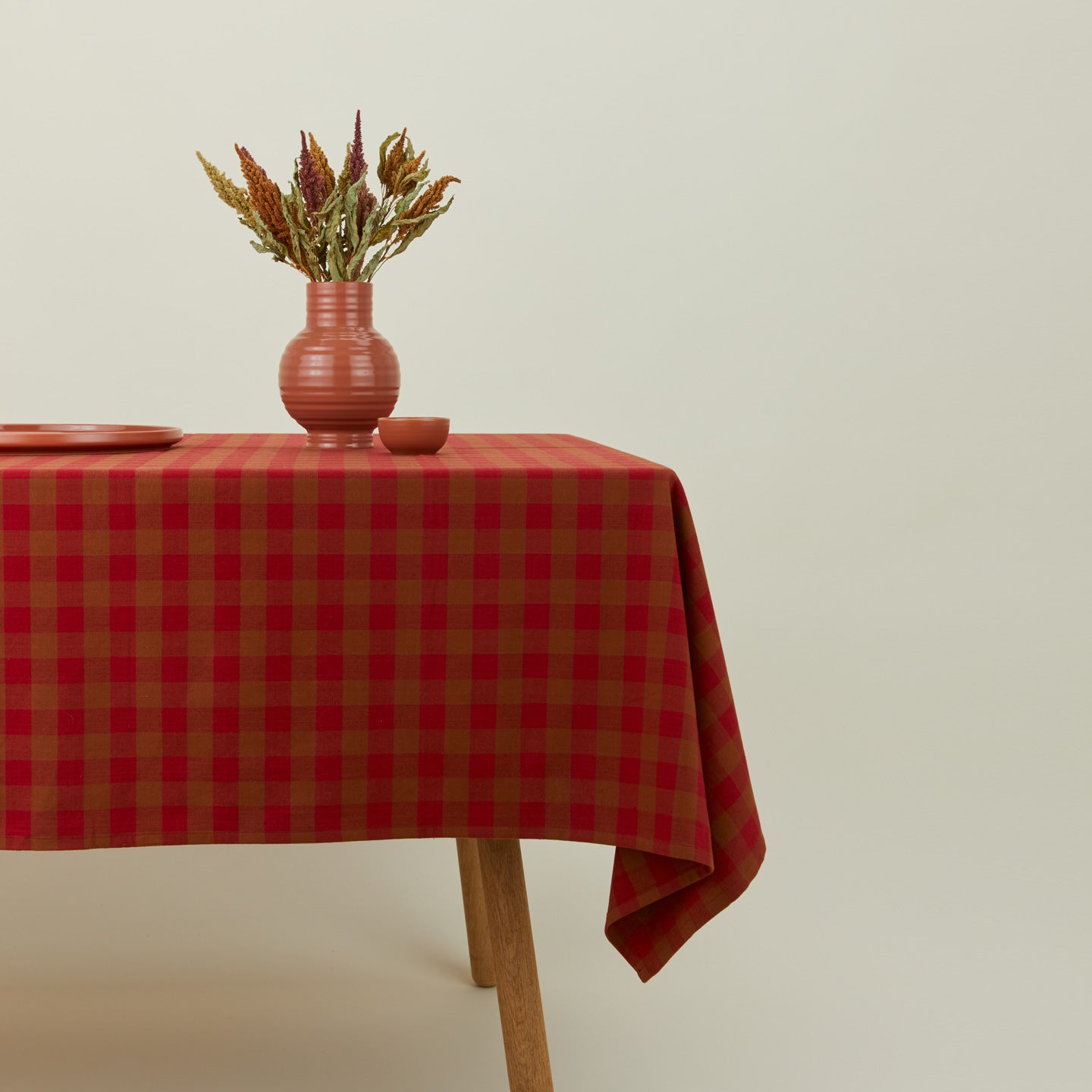 Essential Gingham tablecloth in red/terracotta on a table with florals.