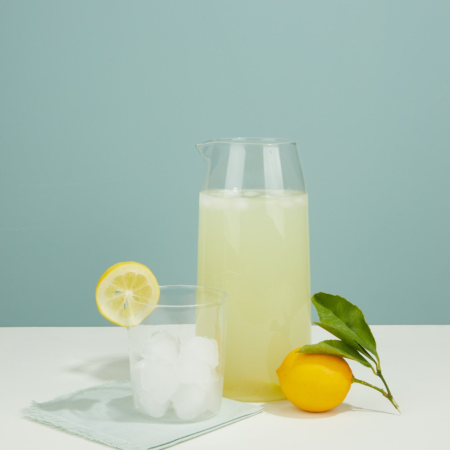 Essential Glass Pitcher and Essential Glass with lemonade and lemon on blue background.