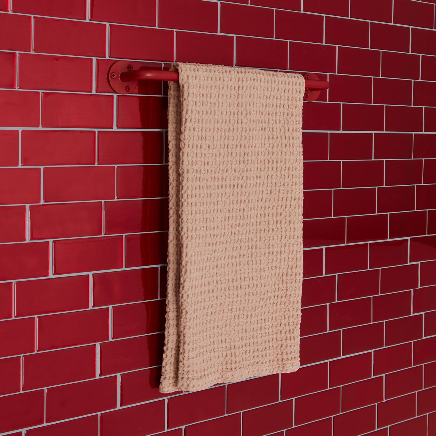 Essential towel bar in red on a tile background.