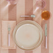 Placesetting with Essential Dinner Napkin in Blush on pink striped tablecloth.