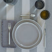 Placesetting with Essential Dinner Napkin in Dark Grey on grey striped tablecloth.