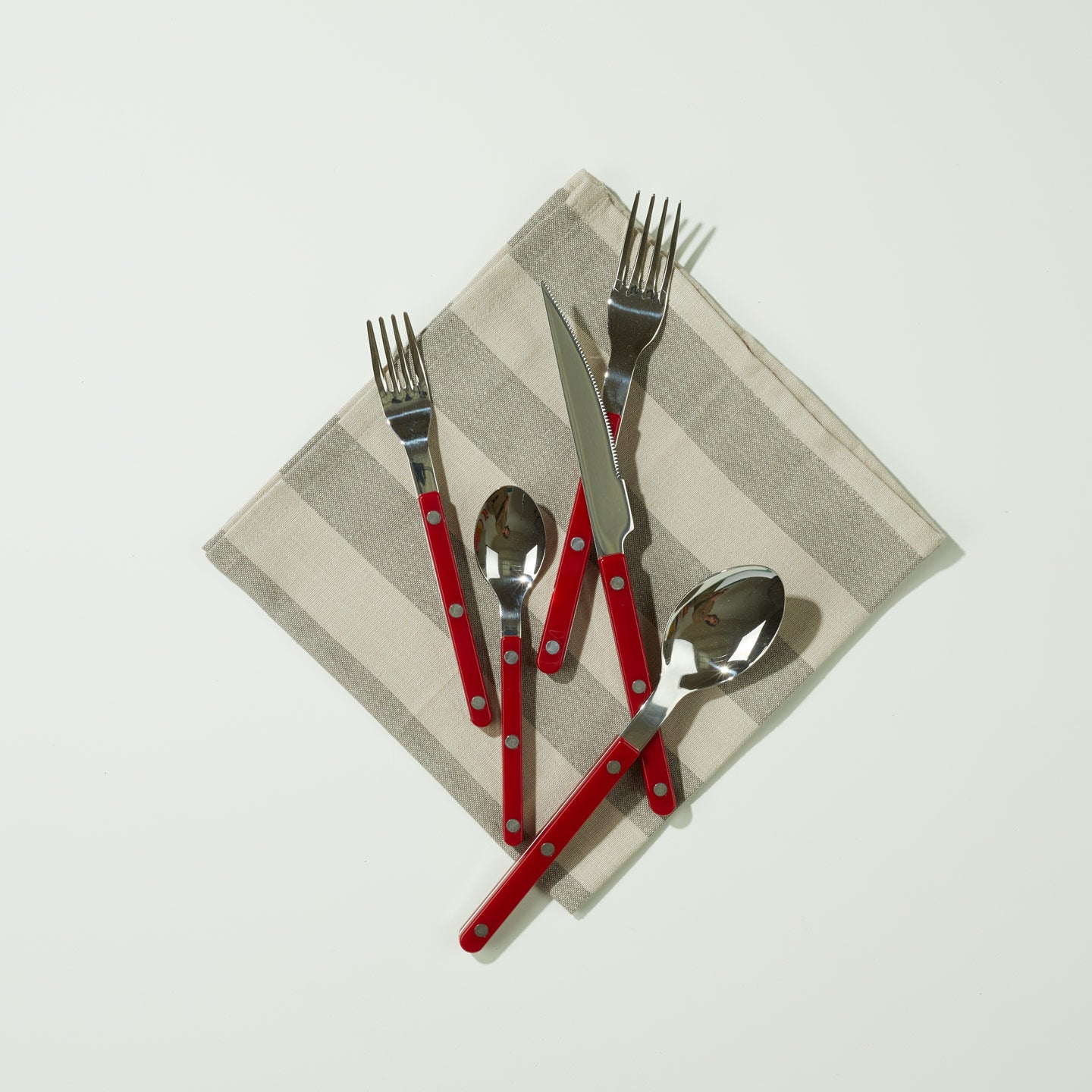 Essential Striped Napkin in Dark and Light Grey with red flatware on light background.