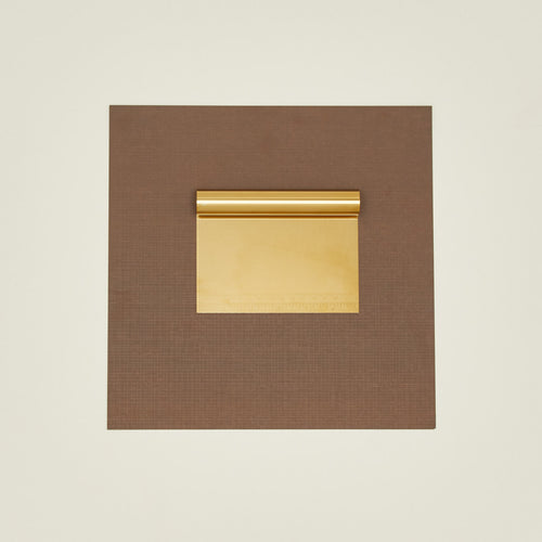 Brass dough scraper on a brown paper on a beige background.