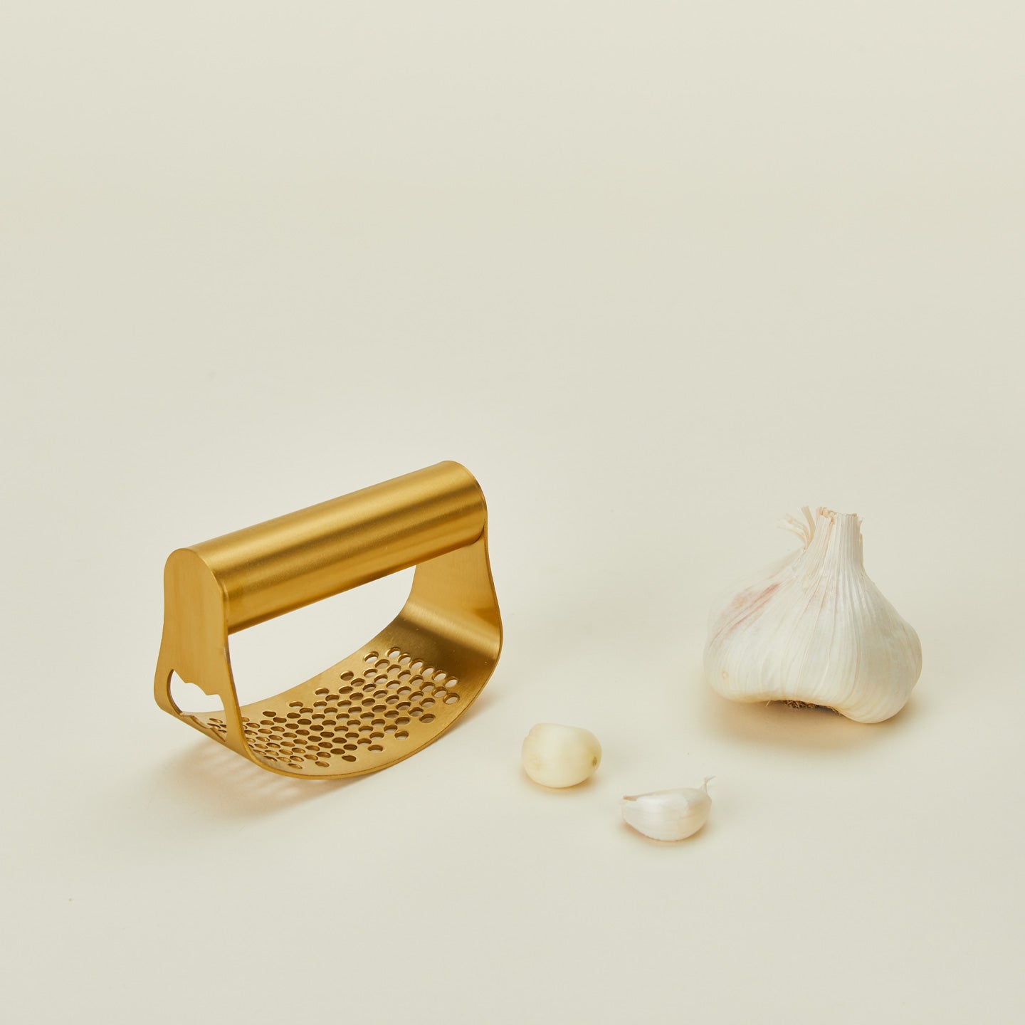 Brass garlic rocker with whole garlic cloves on a beige background