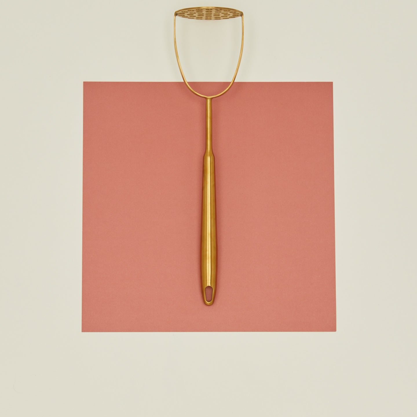 Brass potato masher on pink paper